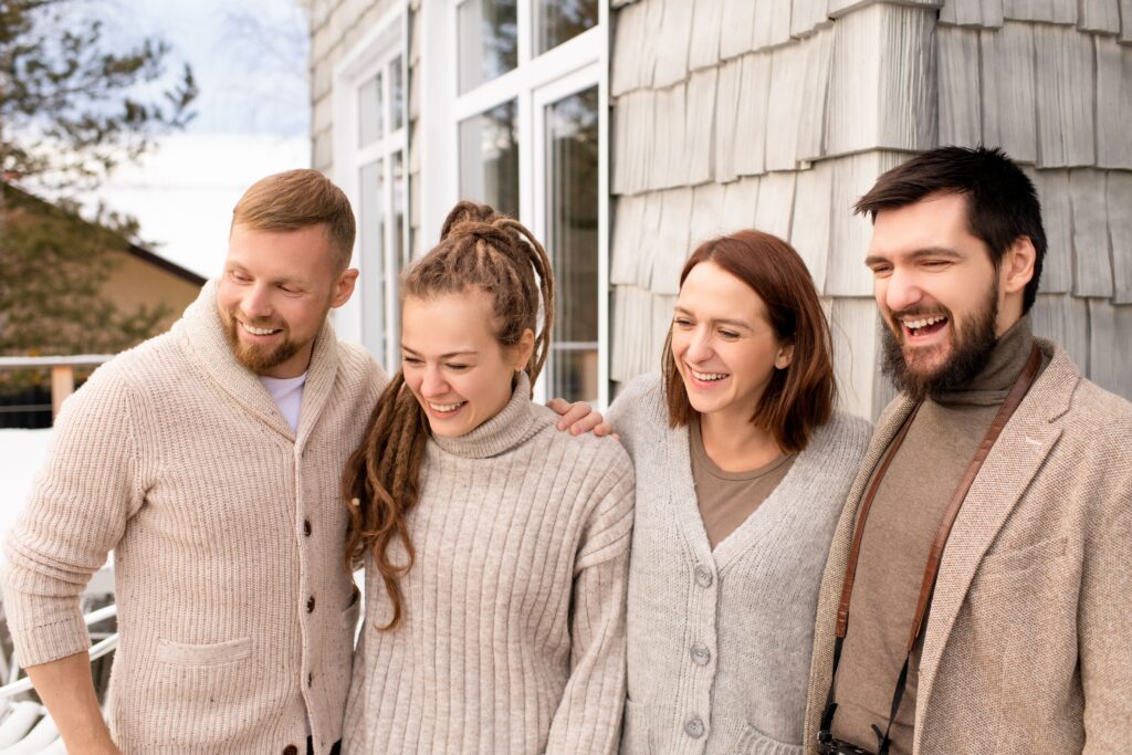 Four friends laughing and bonding outdoors in a cozy winter setting.